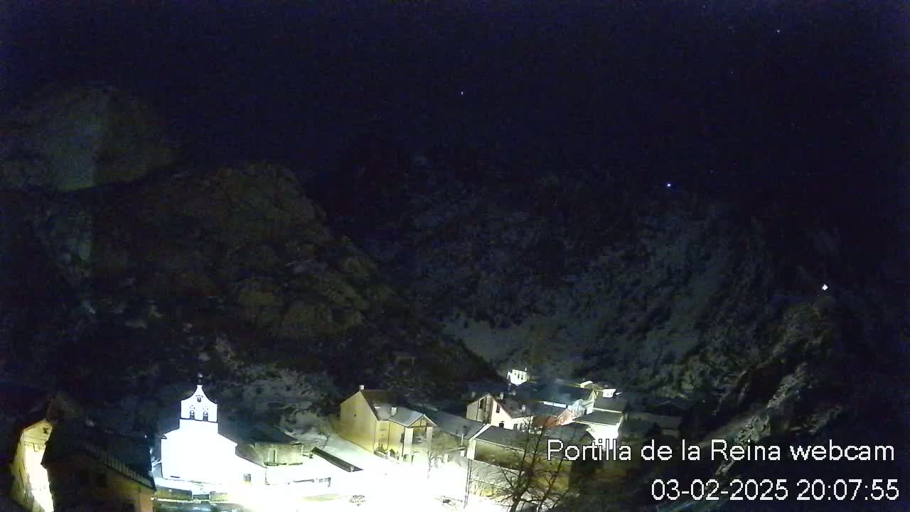 A nighttime view of a small village nestled in a snow-dusted mountain valley under a clear, starry sky.