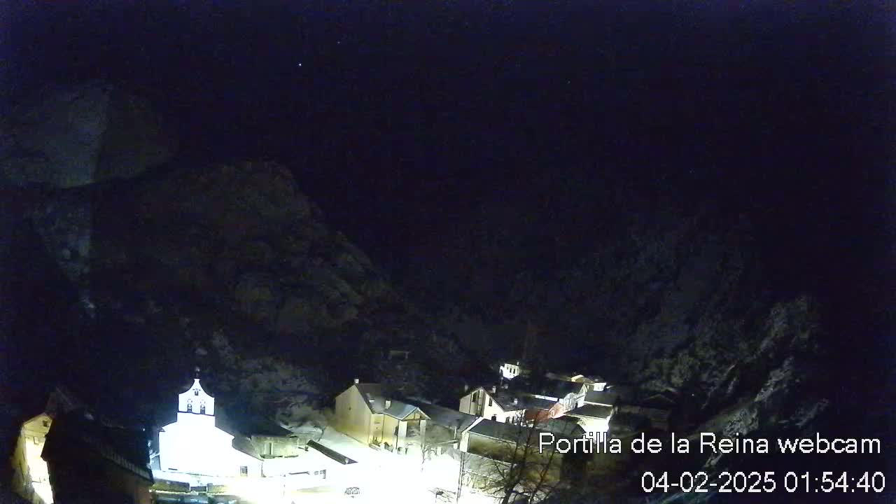 A nighttime view of a small village nestled in a snow-covered mountain valley under a dark, clear sky.