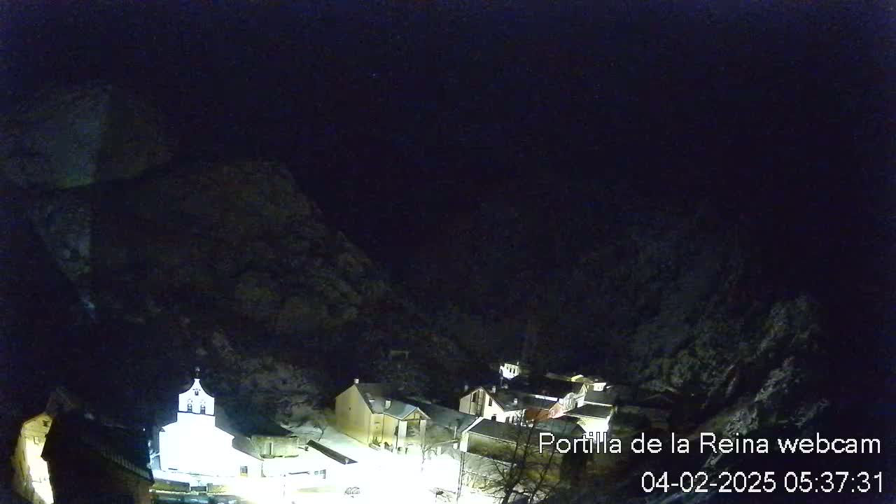 A nighttime, high-angle view of a small village nestled between dark mountains, illuminated by artificial light.