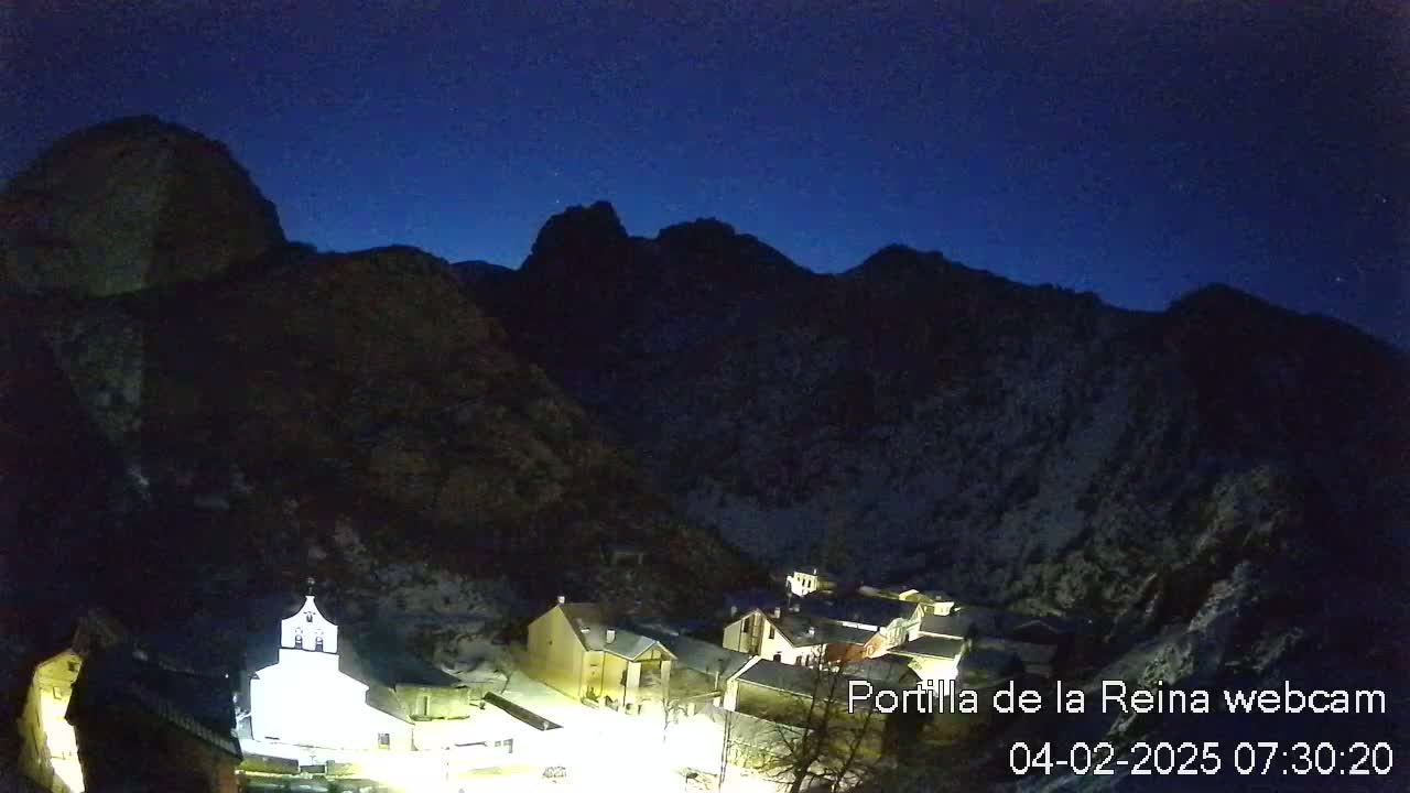 A small village nestled in a valley between dark, snow-dusted mountains under a twilight sky.