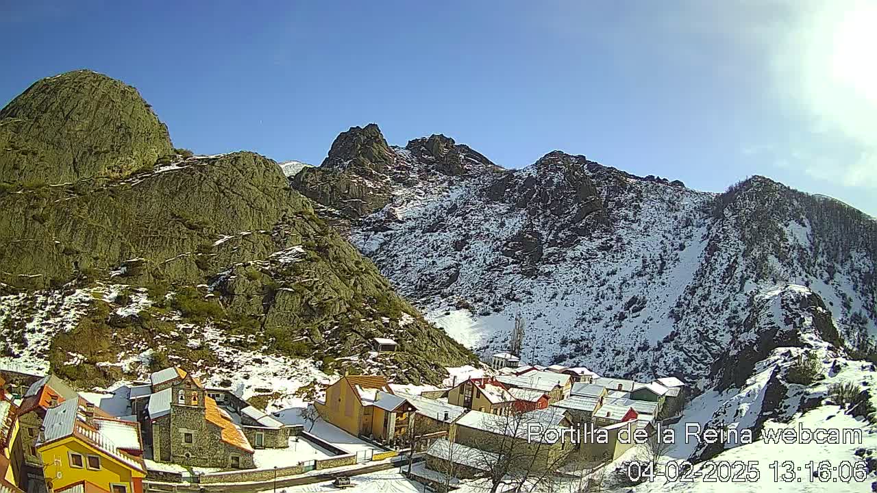 A small village nestled in a valley between snow-dusted mountains under a clear blue sky.