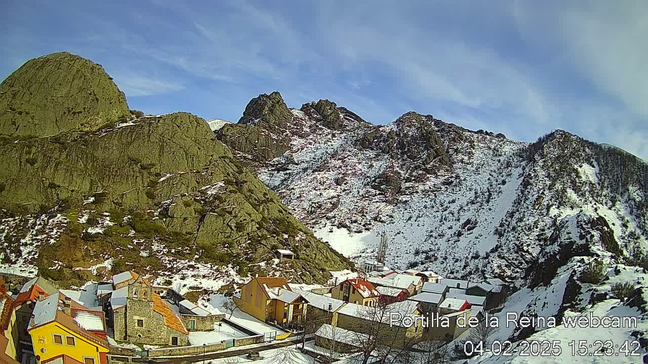 A small village nestled in a snow-dusted mountain valley under a mostly sunny sky.