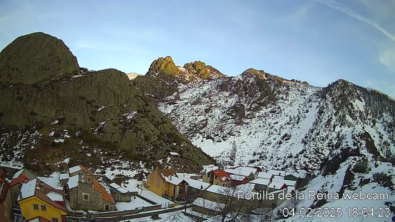 A snow-covered village nestled in a valley between rocky mountains under a clear blue sky.