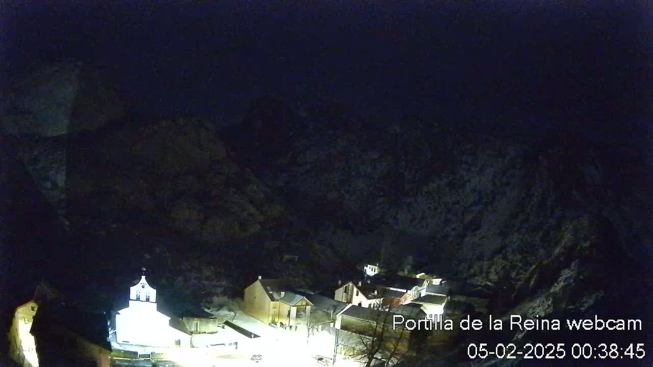 A nighttime view of a small village nestled in a snow-dusted mountain valley under a dark sky.