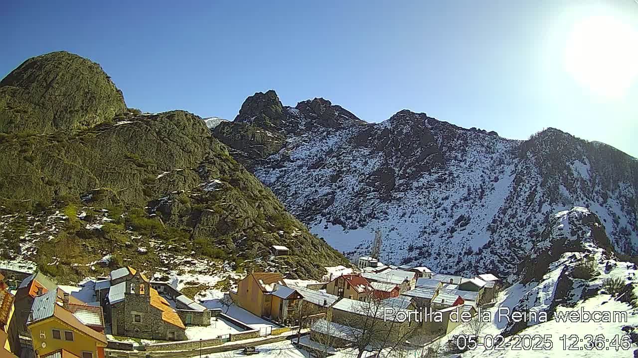 A small village nestled in a valley between snow-dusted mountains under a clear, sunny sky.