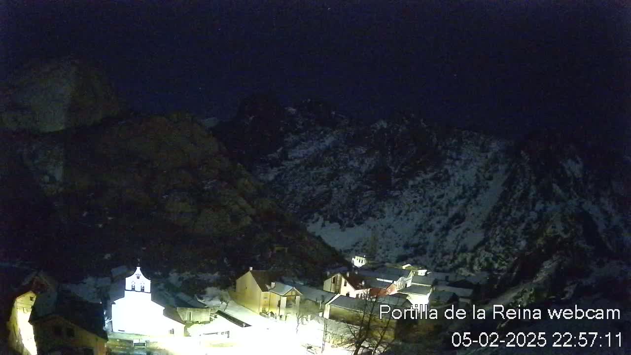 A nighttime view of a small village nestled in a snow-dusted mountain valley under a dark, clear sky.