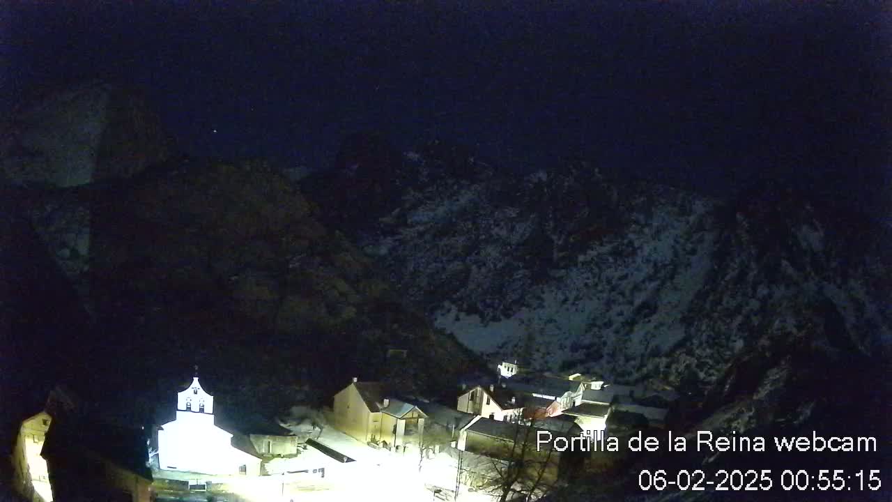 A nighttime view of a small village nestled in a snow-dusted mountain valley under a dark, clear sky.