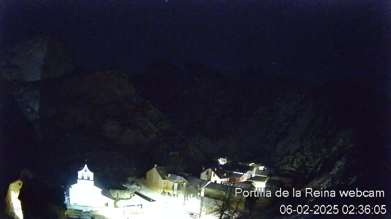 A nighttime view of a small village nestled in a valley surrounded by dark mountains under a clear, starlit sky.