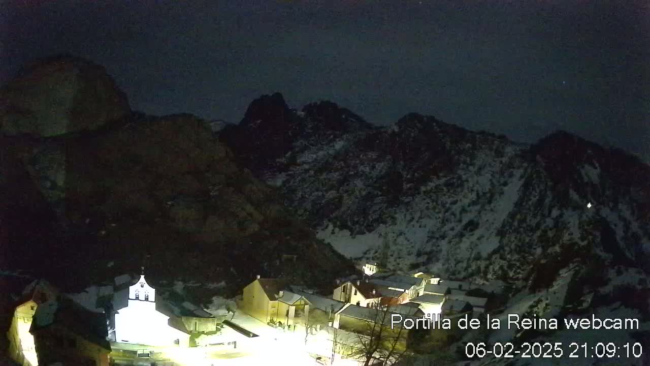 A snow-dusted mountain village is nestled in a valley under a dark night sky.