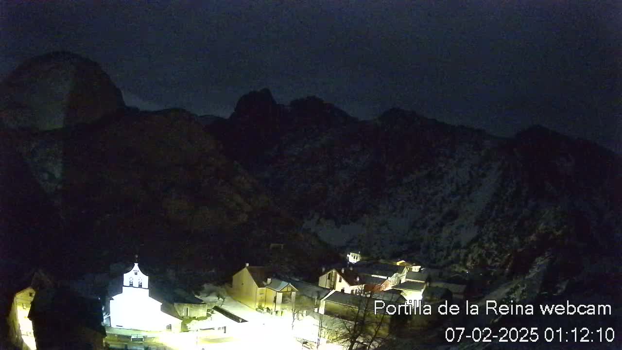 A small, snow-dusted village nestled in a dark, mountainous valley under a night sky.
