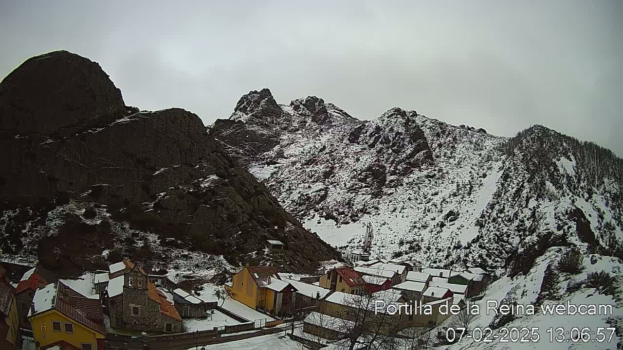 A small village nestled in a snow-covered mountain valley under an overcast sky.