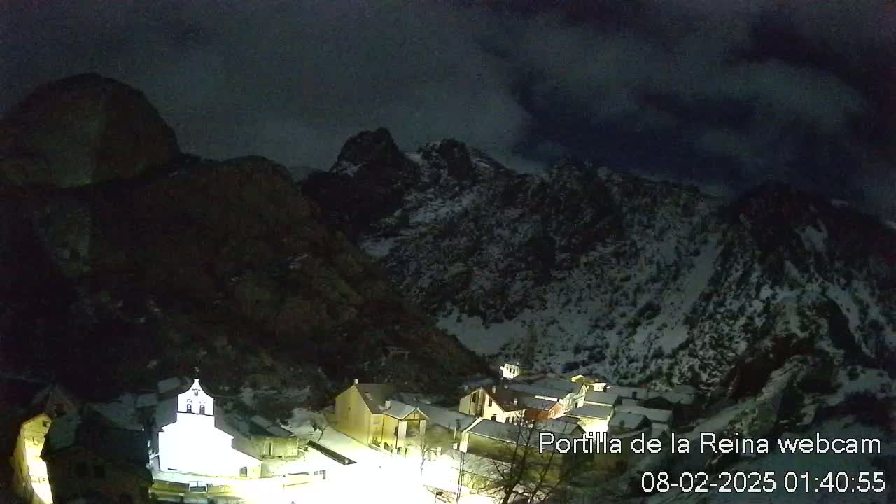 A small village nestled in a snow-dusted mountain valley under a dark, cloudy night sky.