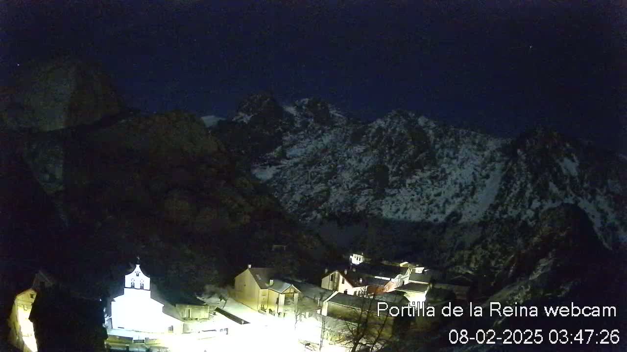 A small village nestled at the base of snow-capped mountains under a dark, clear night sky.