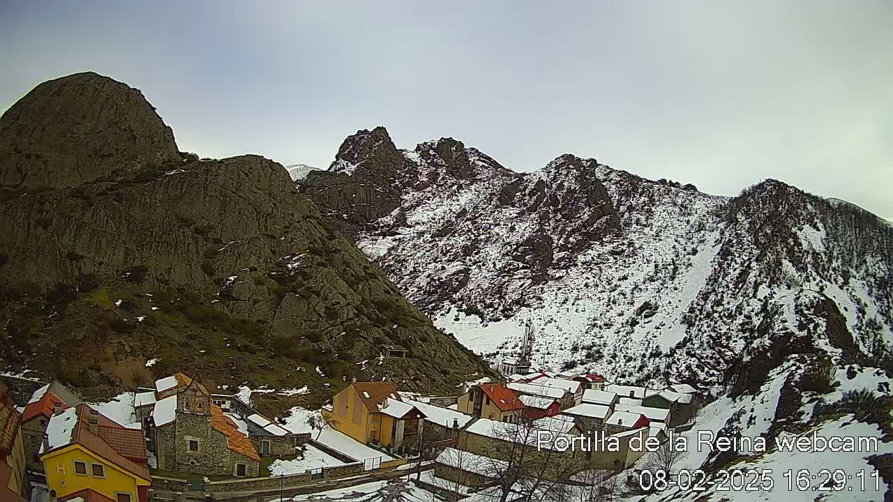 A small village nestled in a valley between snow-dusted mountains under an overcast sky.