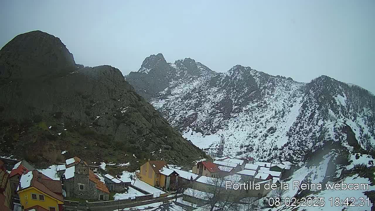 A snow-dusted village nestled in a valley between steep, rocky mountains under an overcast sky.