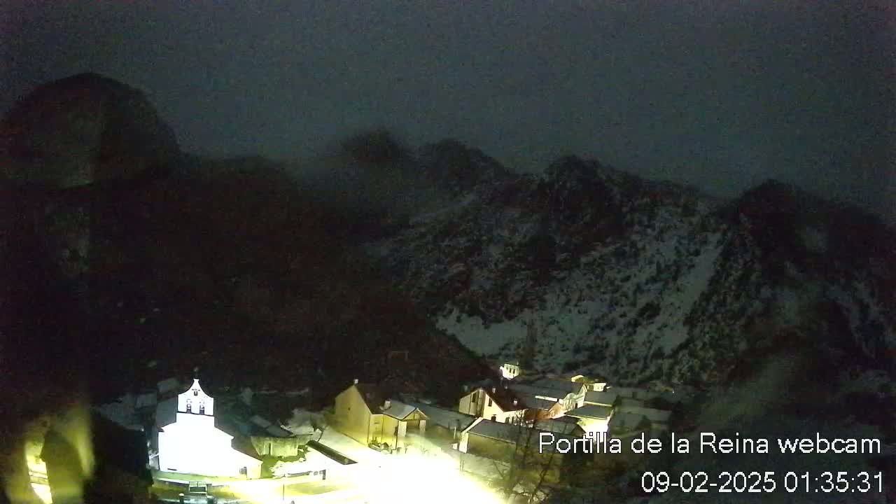 A nighttime view of a small village nestled in a snow-dusted mountain valley under a dark sky.