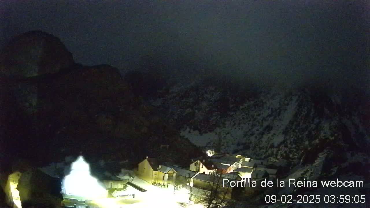 A nighttime, snow-covered mountain village is shrouded in fog under a dark sky.
