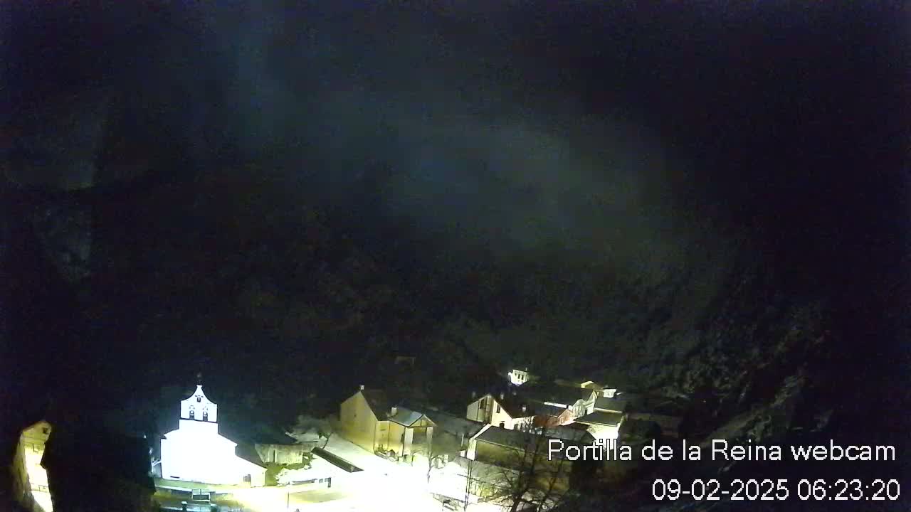A nighttime, snow-covered village nestled in a dark, mountainous valley under a cloudy sky.