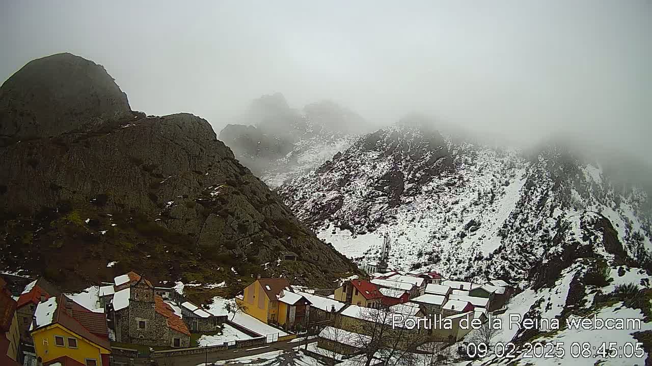 A small village nestled in a snow-dusted mountain valley shrouded in fog.