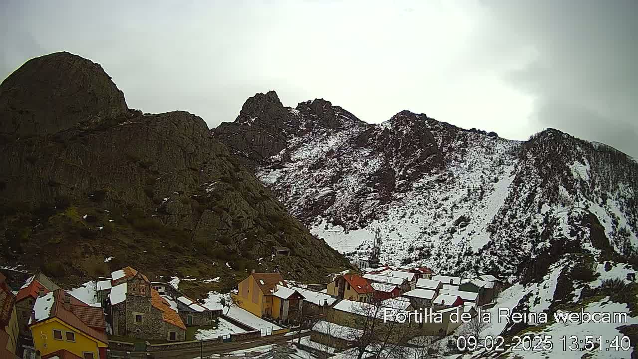A small village nestled in a valley between snow-dusted mountains under an overcast sky.