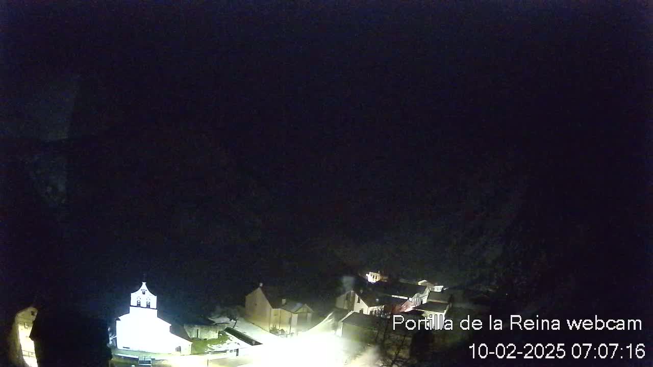 A nighttime, high-angle view of a small village with a brightly lit church, under a dark sky.