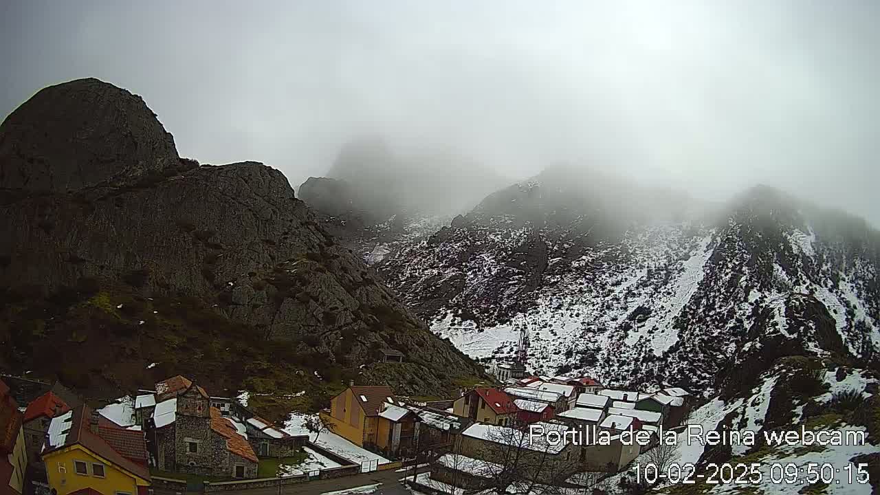A small village nestled in a valley between snow-dusted mountains shrouded in fog.