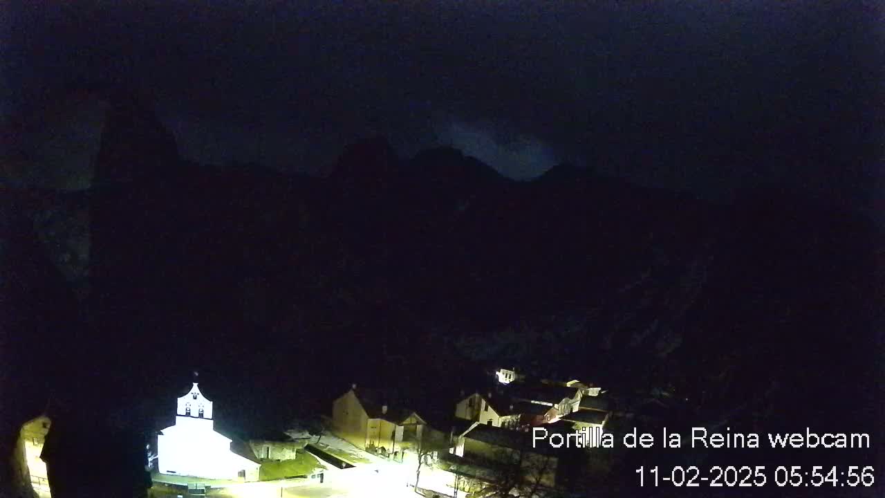 A small, dimly lit village nestled at the base of dark, mountainous terrain under a nighttime sky.