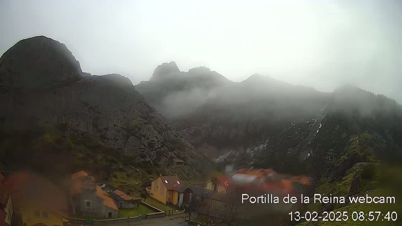A foggy, overcast day reveals a village nestled at the base of a rocky mountain range.