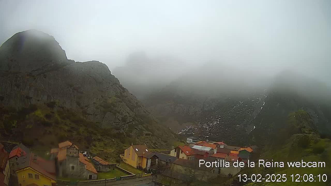 A foggy mountain village nestled in a valley between steep, rocky mountains.