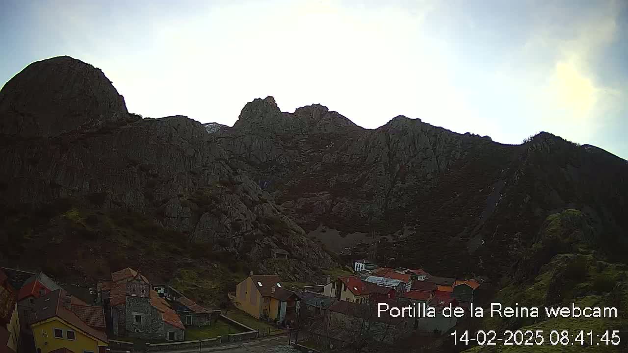 A small village nestled at the base of a large, dark mountain range under a mostly clear sky.