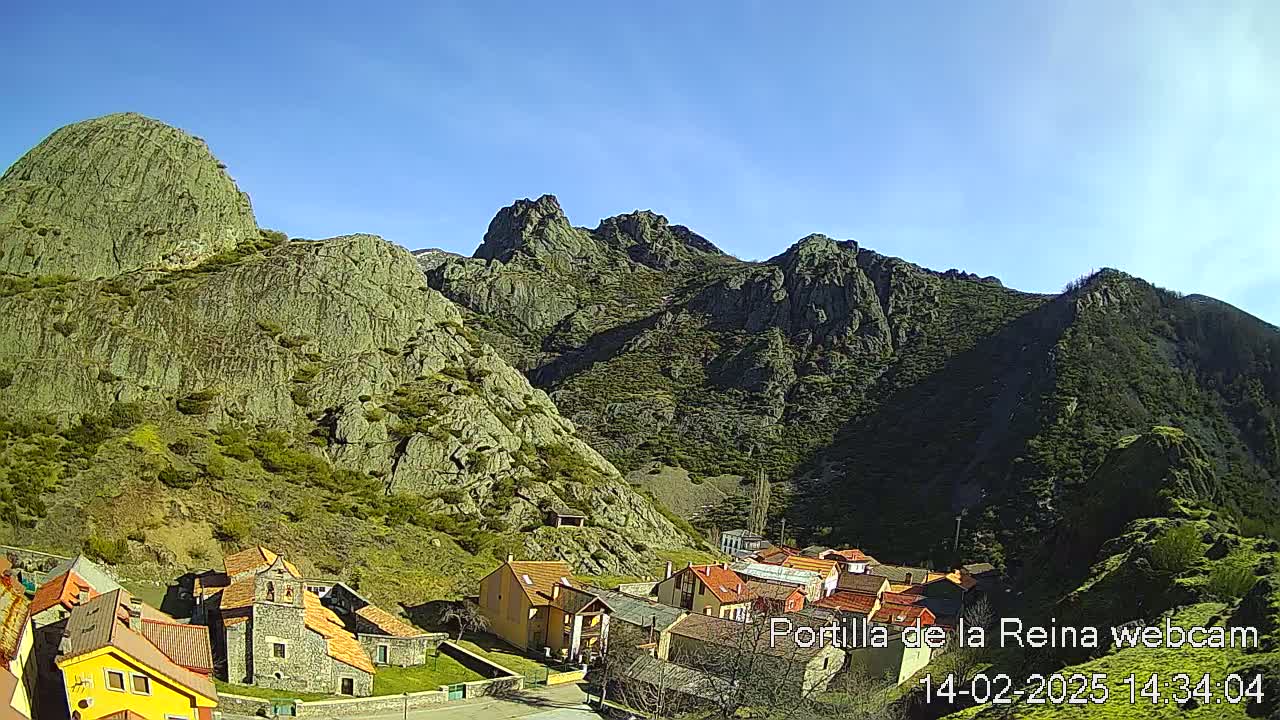 A small village nestled in a valley between large, rocky mountains under a clear blue sky.
