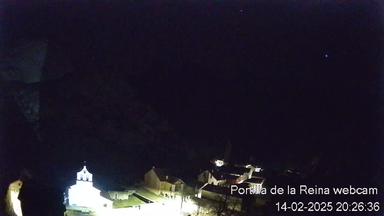 A nighttime view of a small village nestled against a dark mountainside under a clear, starlit sky.