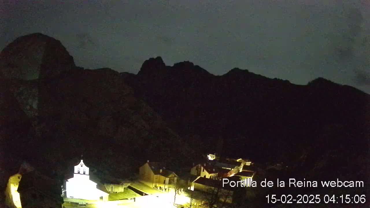 A small, illuminated village nestled at the base of dark mountains under a nighttime sky.