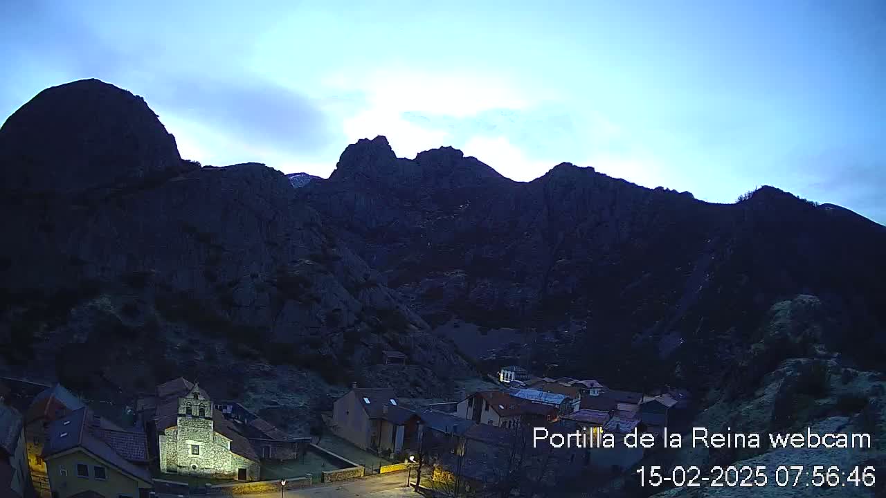A small village nestled in a valley between dark, rocky mountains under a twilight sky.