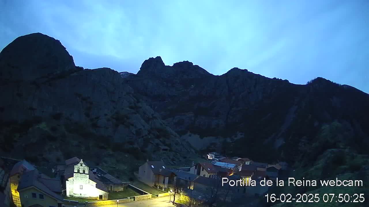 A small village nestled in a valley between dark, rocky mountains under a twilight sky.