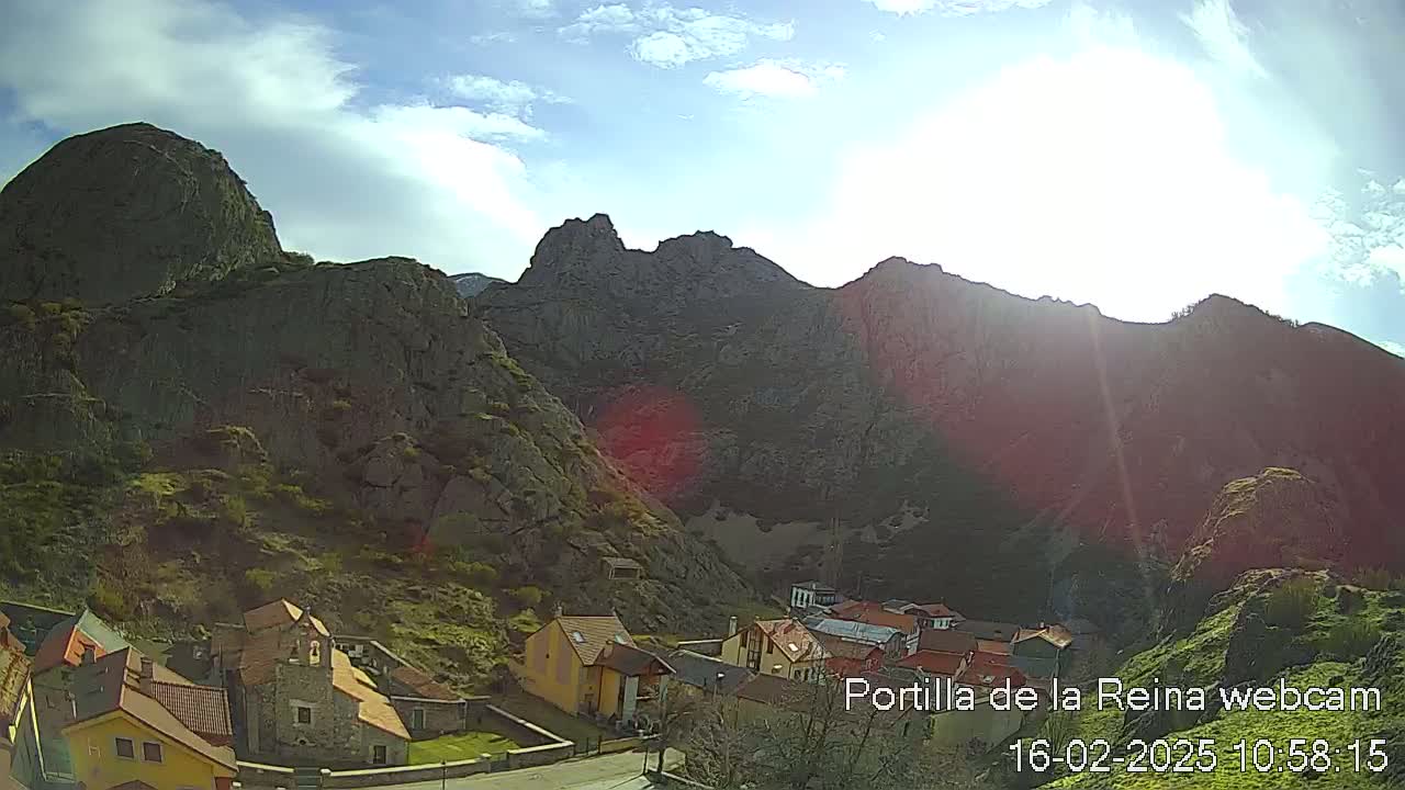 A small village nestled in a valley surrounded by large, rocky mountains under a partly sunny sky.
