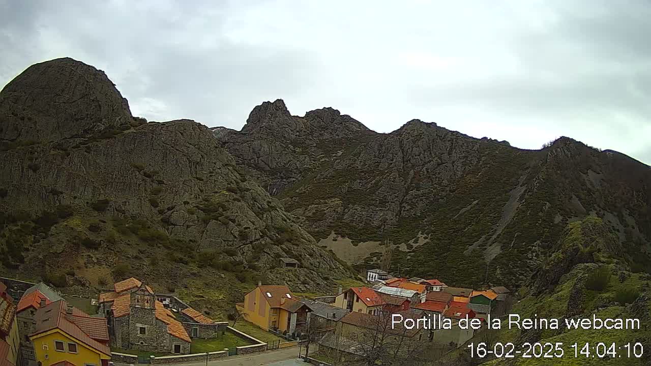 A small village nestled in a valley between large, rocky mountains under an overcast sky.