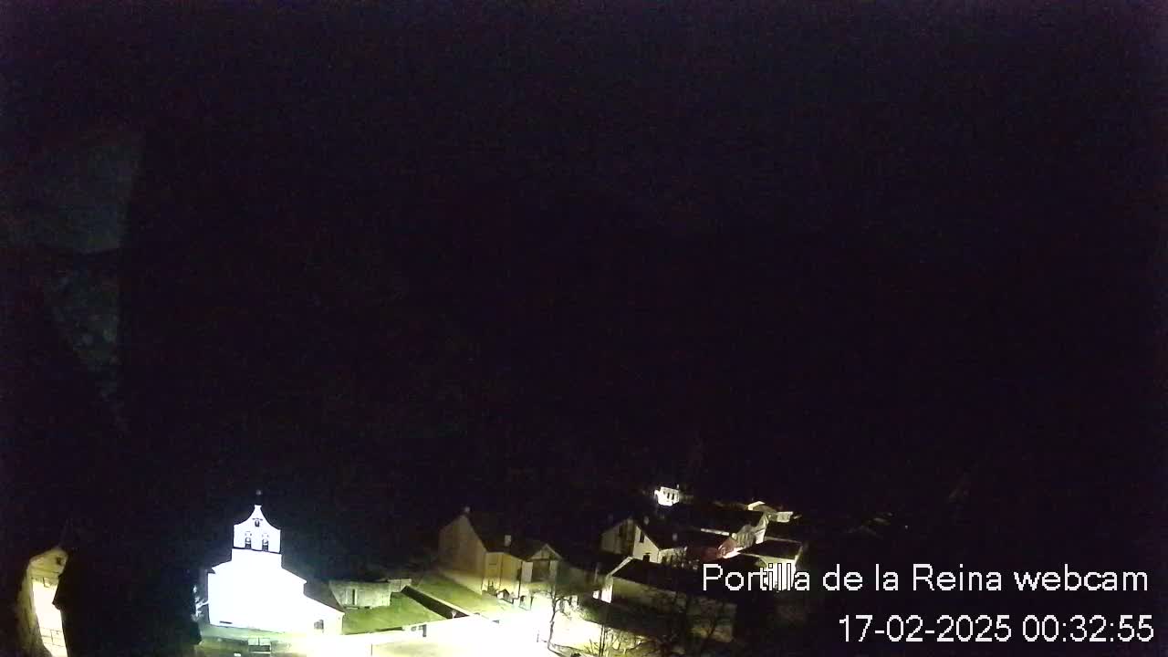 A nighttime, overhead view of a small village with a brightly lit church, under a dark sky.