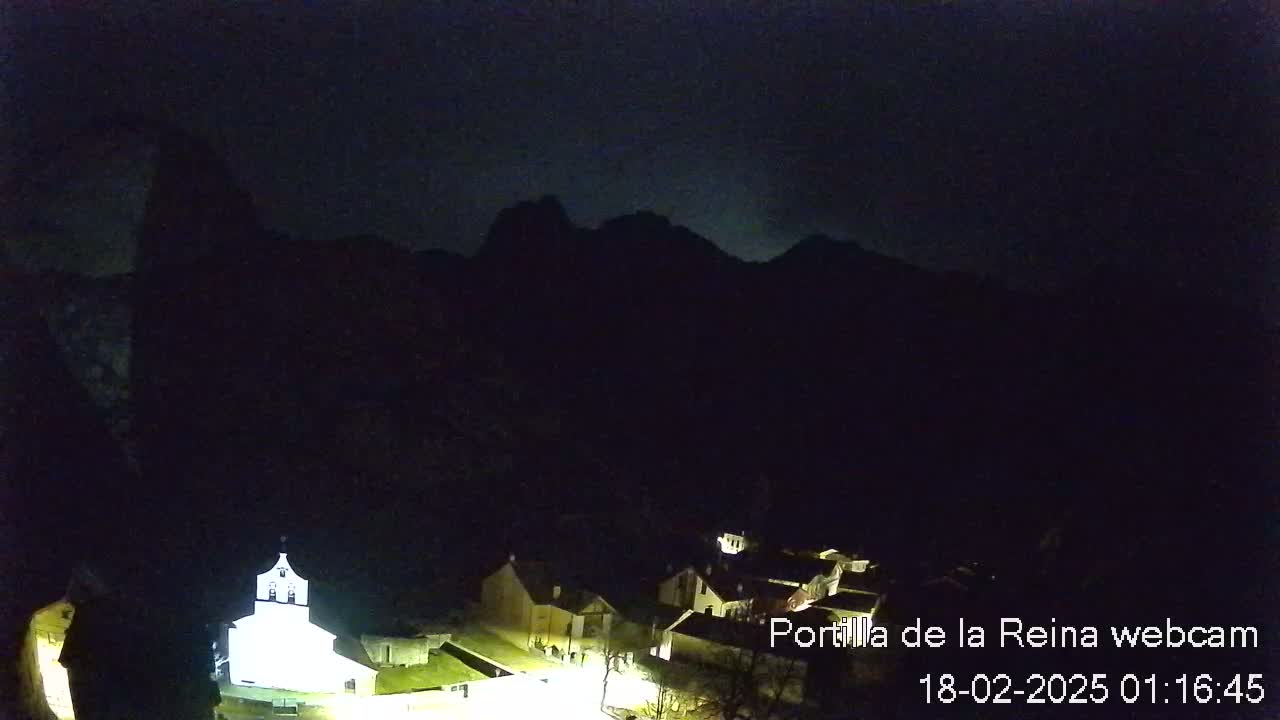 A small, dimly lit village nestled at the base of dark mountains under a nighttime sky.