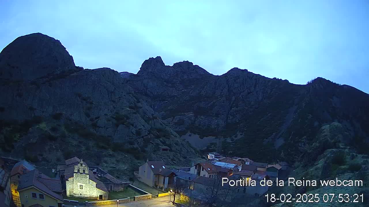 A small village nestled at the base of a large, dark mountain range under a twilight sky.