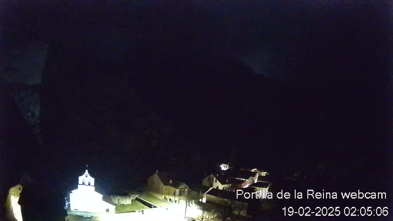 A nighttime, overhead view of a small village nestled at the base of a dark mountain.