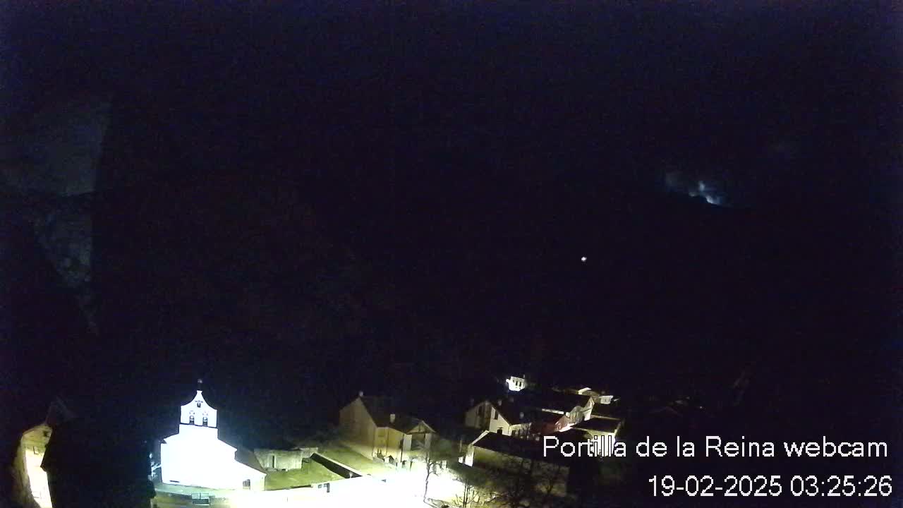 A nighttime long shot of a small village illuminated by artificial lights under a dark, clear sky.