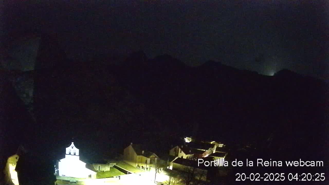 A small, dimly lit village nestled at the base of dark mountains under a nighttime sky.
