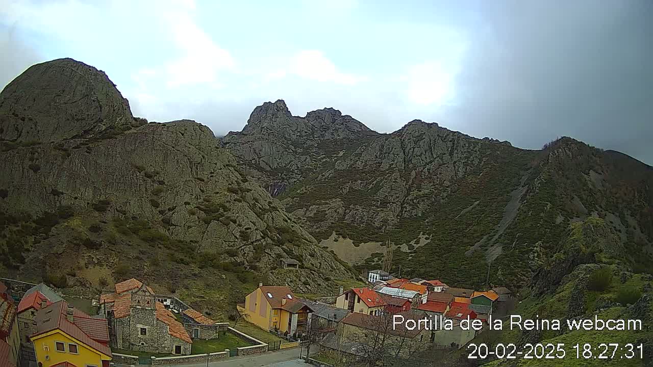A small village nestled in a valley surrounded by large, rocky mountains under an overcast sky.