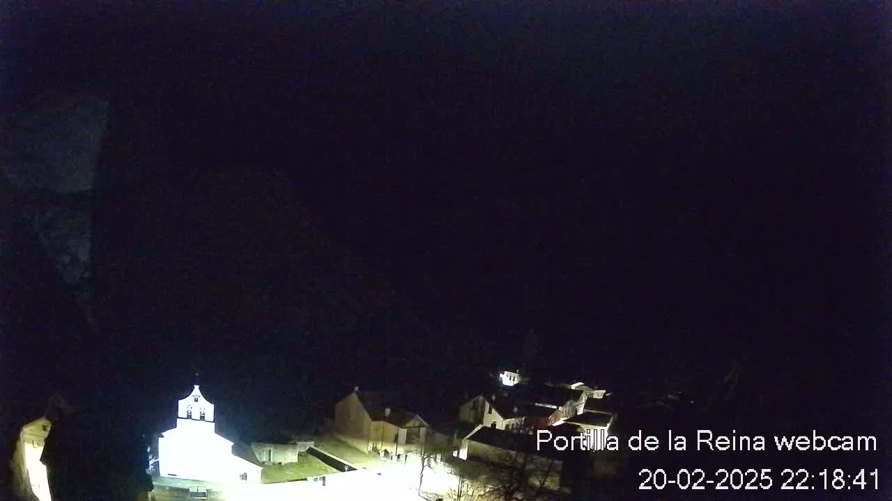 A nighttime, high-angle view of a small village with a brightly lit church, under a dark sky.