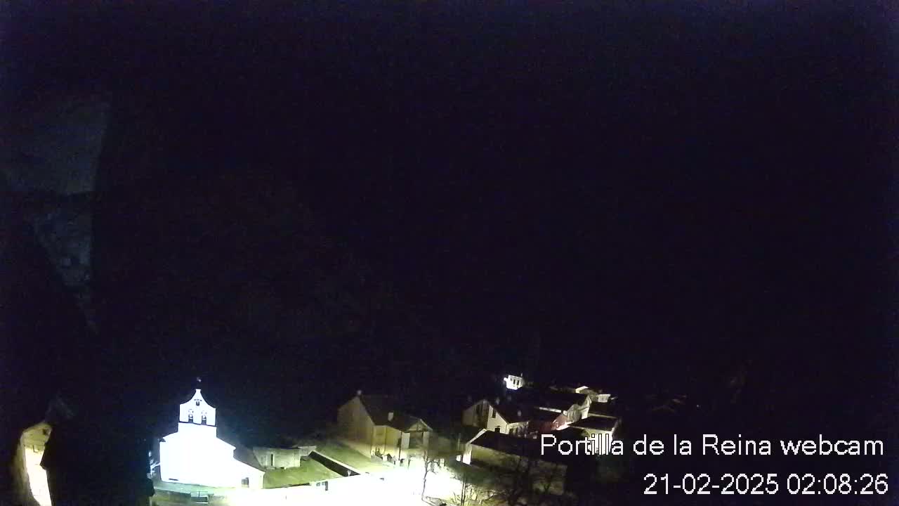 A dimly lit, nighttime view of a small village nestled against a dark hillside.