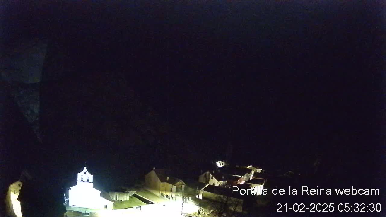 A nighttime, high-angle view of a small village illuminated by artificial light, nestled in a dark, mountainous area.