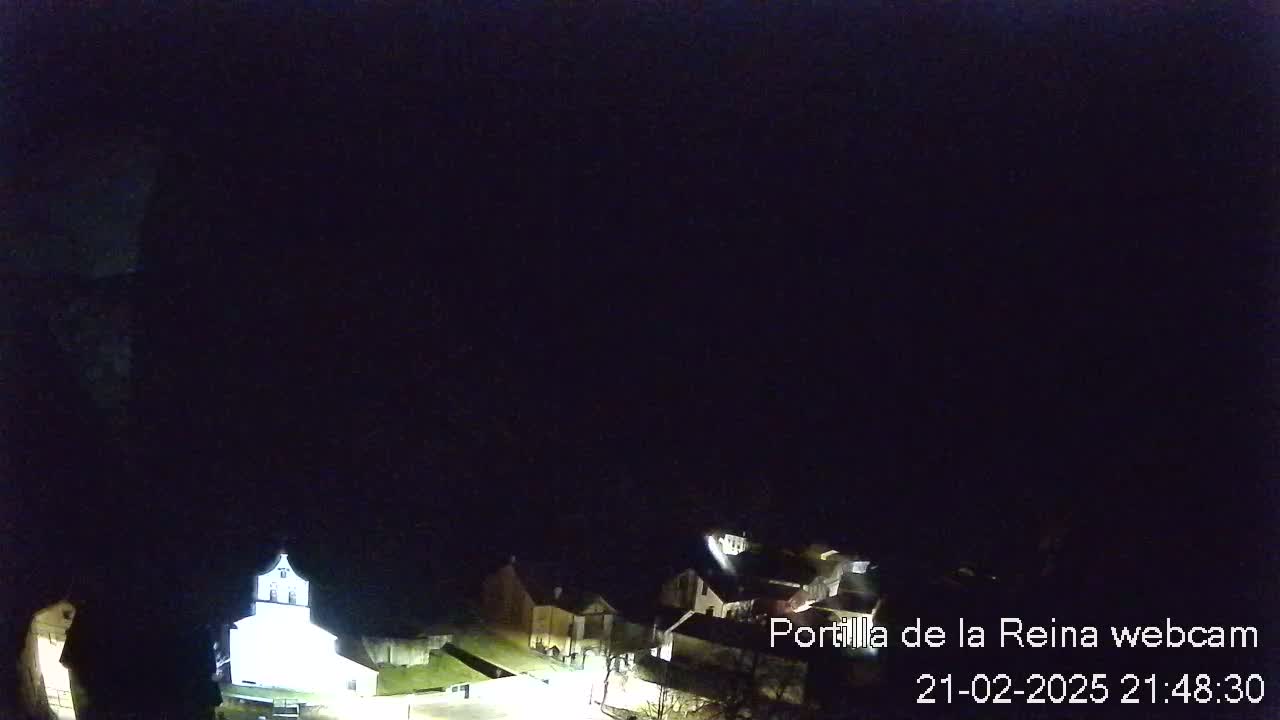 A nighttime, overhead view shows a small village with dimly lit buildings under a dark, clear sky.