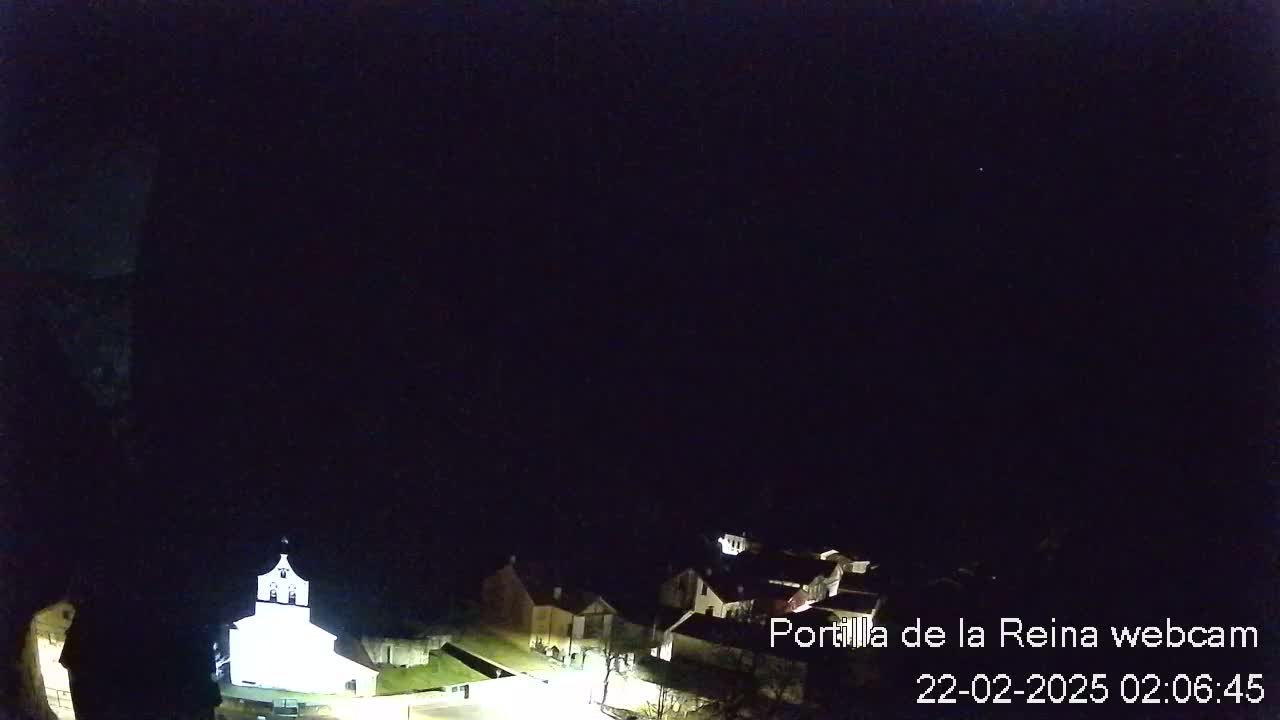 A nighttime, high-angle view shows a small village with a brightly lit church, under a clear, dark sky.