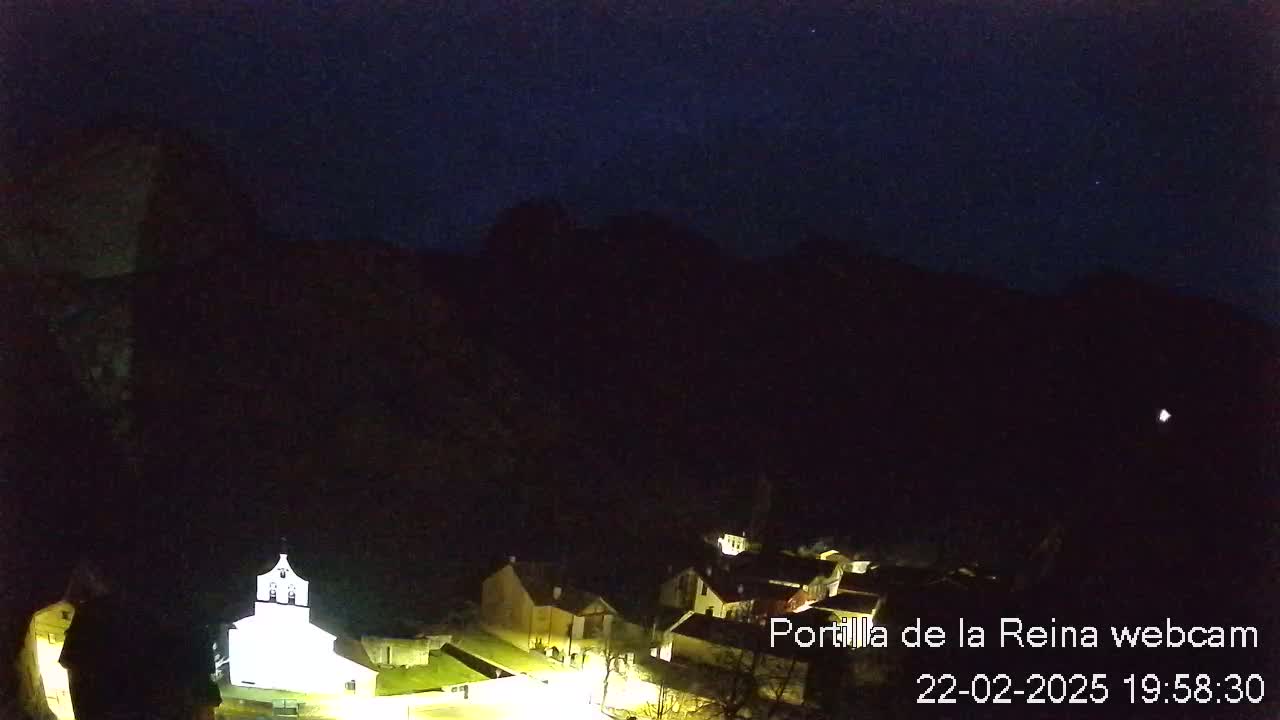 A small, illuminated village nestled in a dark, mountainous valley under a clear, starlit night sky.